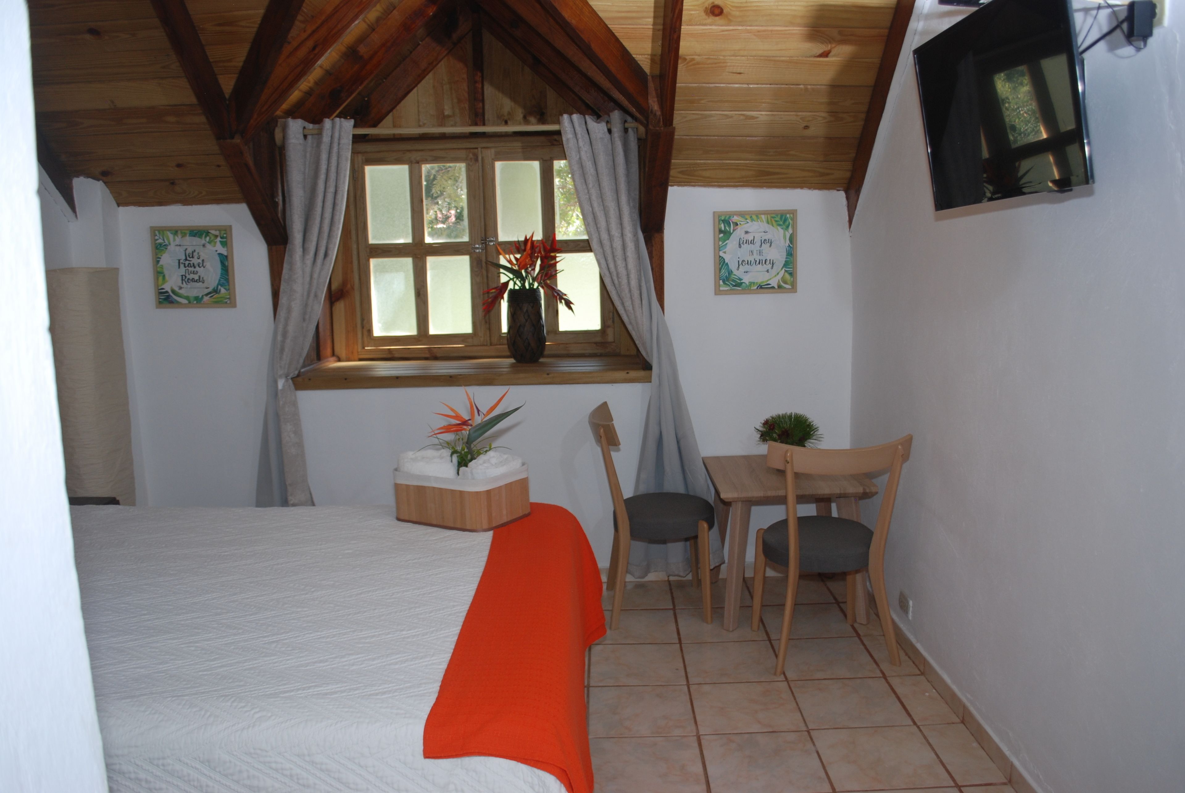 A bedroom with a bed, a desk, and a chair. There is a window with curtains and a plant on the windowsill.