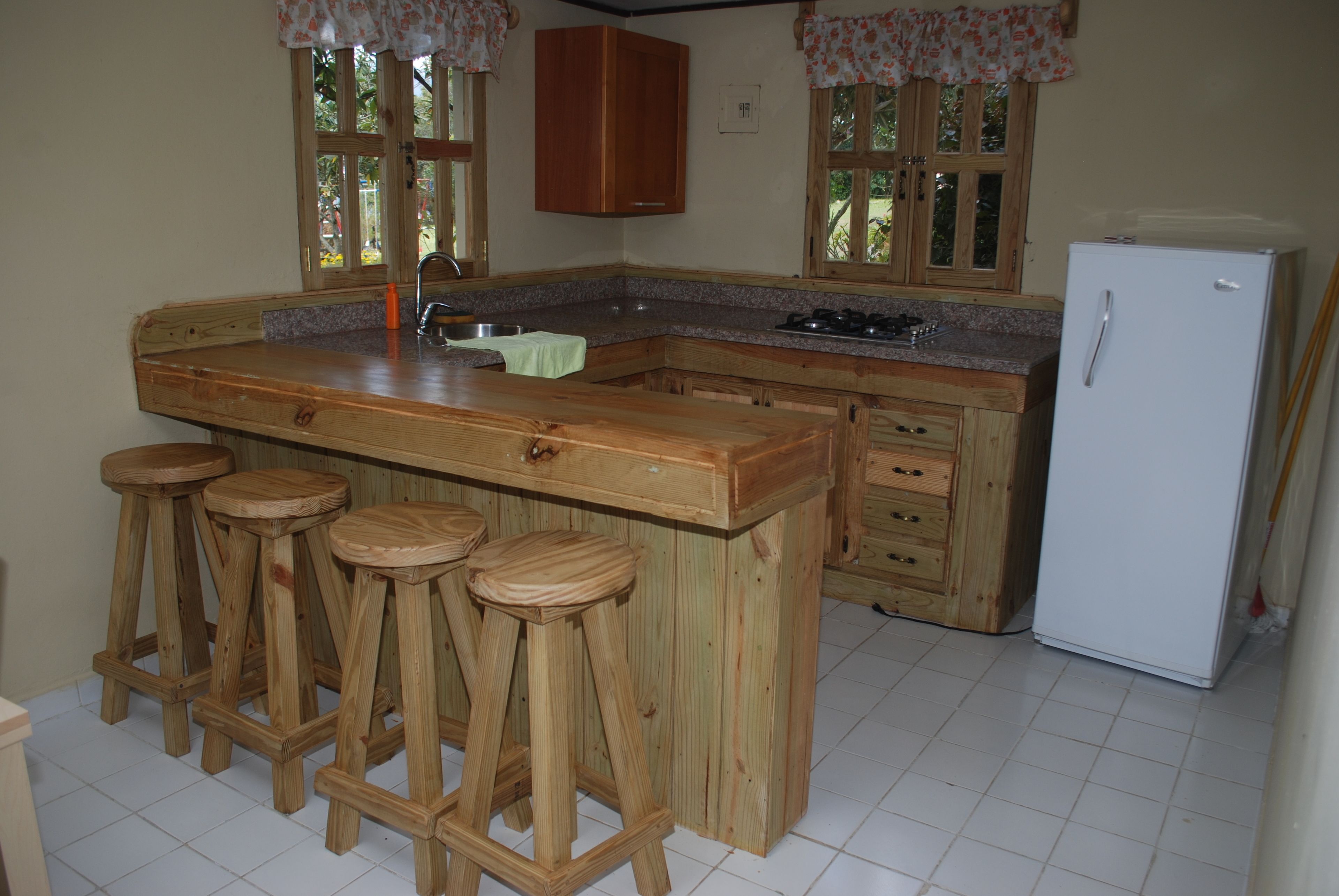 A kitchen with wooden bar stools, a white refrigerator, and wooden cabinets.