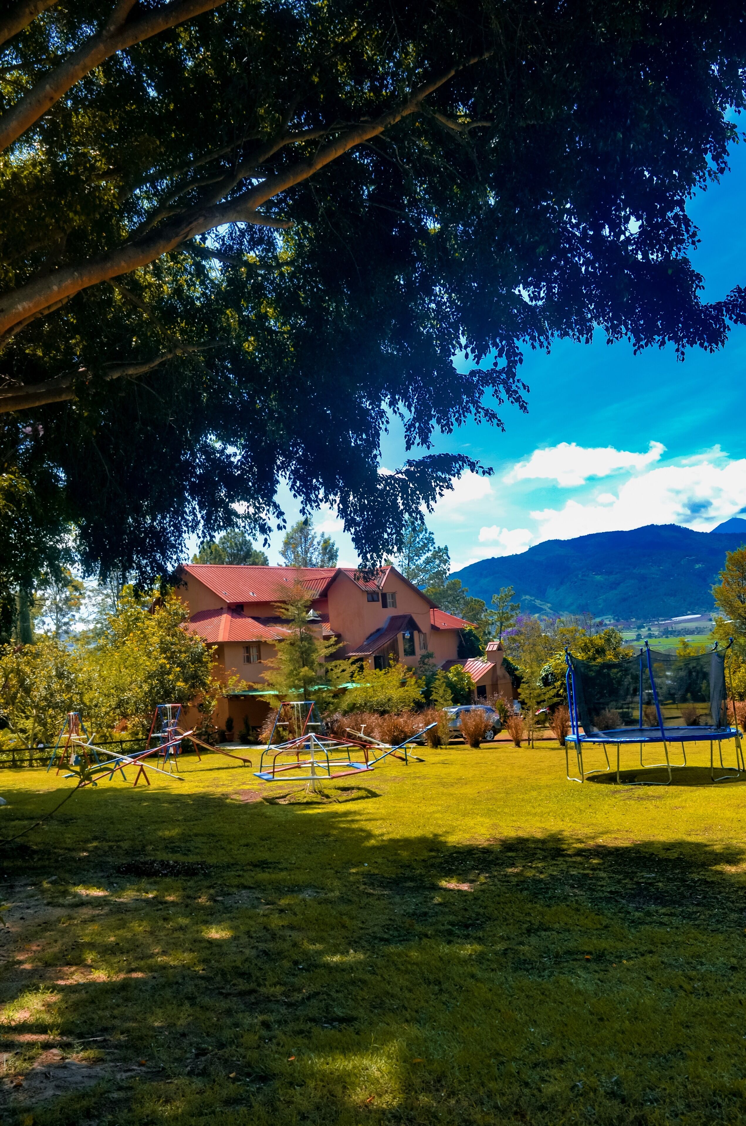 A house with a red roof, surrounded by a grassy yard with playground equipment.