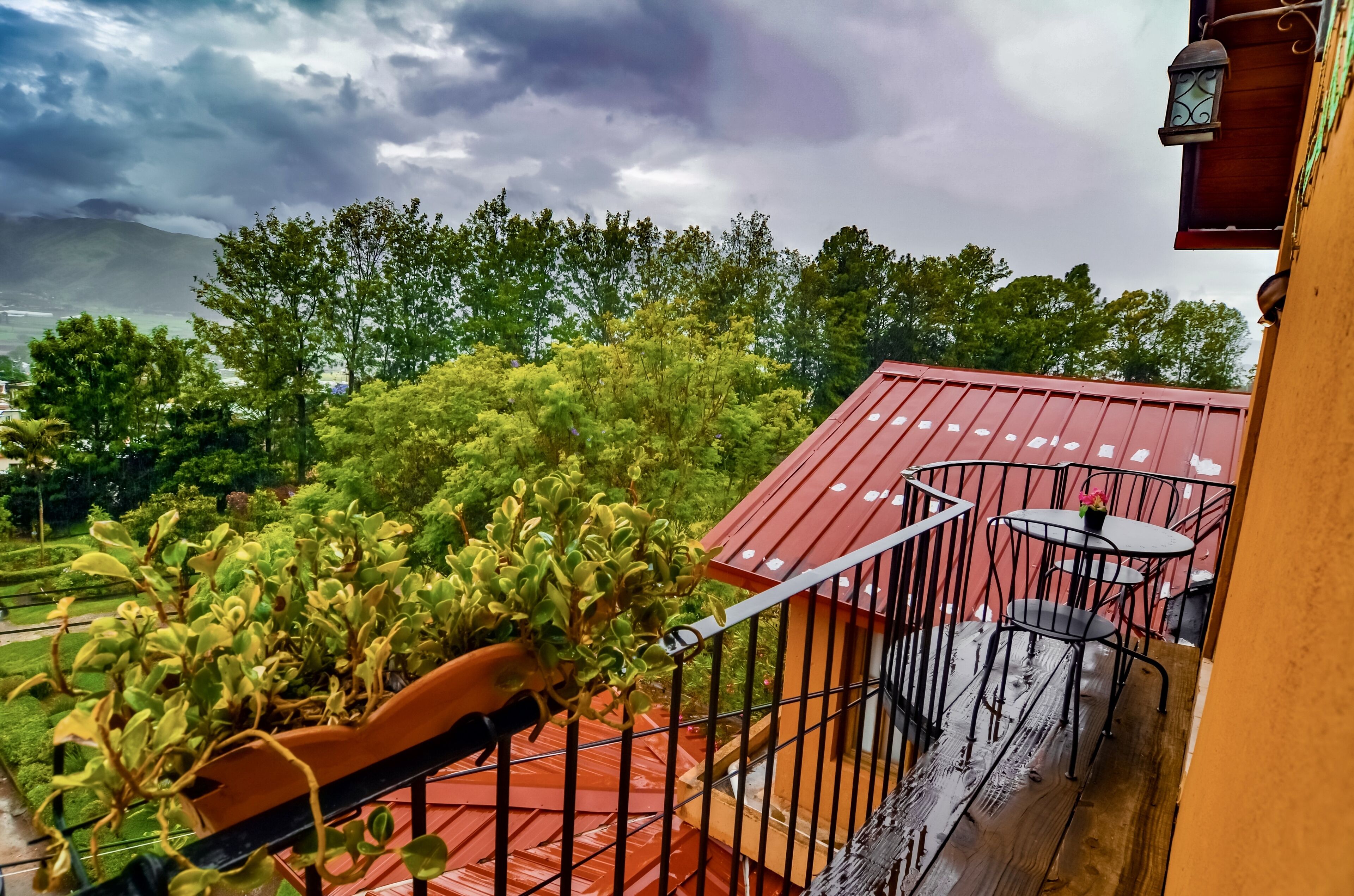 A balcony with a red roof, a small table and chairs, and a potted plant.