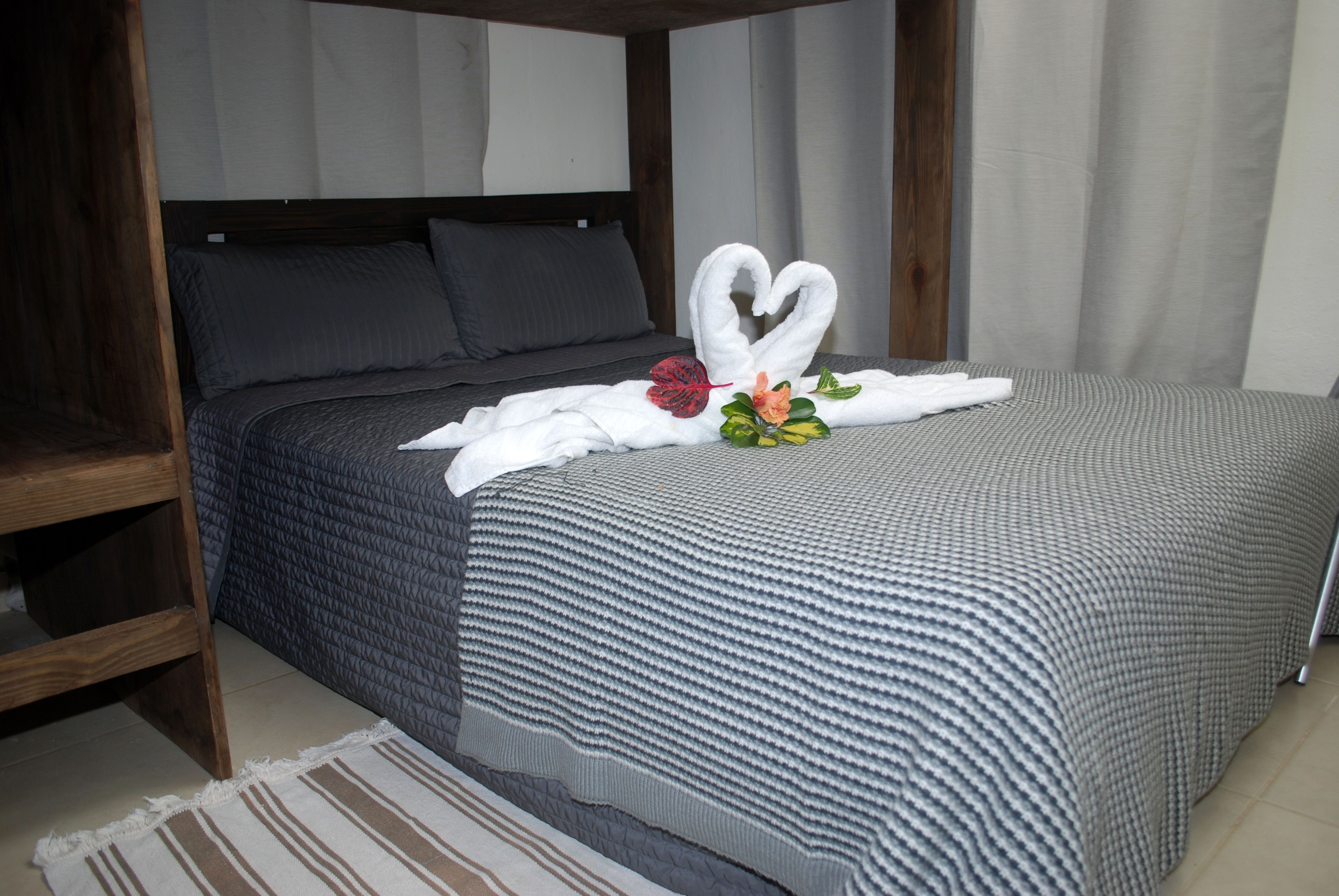Una cama bien hecha con una decoración de toallas en forma de corazón, un cabecero de madera y una alfombra a rayas.
