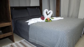 Una cama bien hecha con una decoración de toallas en forma de corazón, un cabecero de madera y una alfombra a rayas.