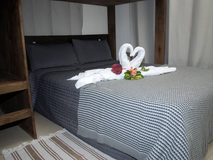 Una cama bien hecha con una decoración de toallas en forma de corazón, un cabecero de madera y una alfombra a rayas.