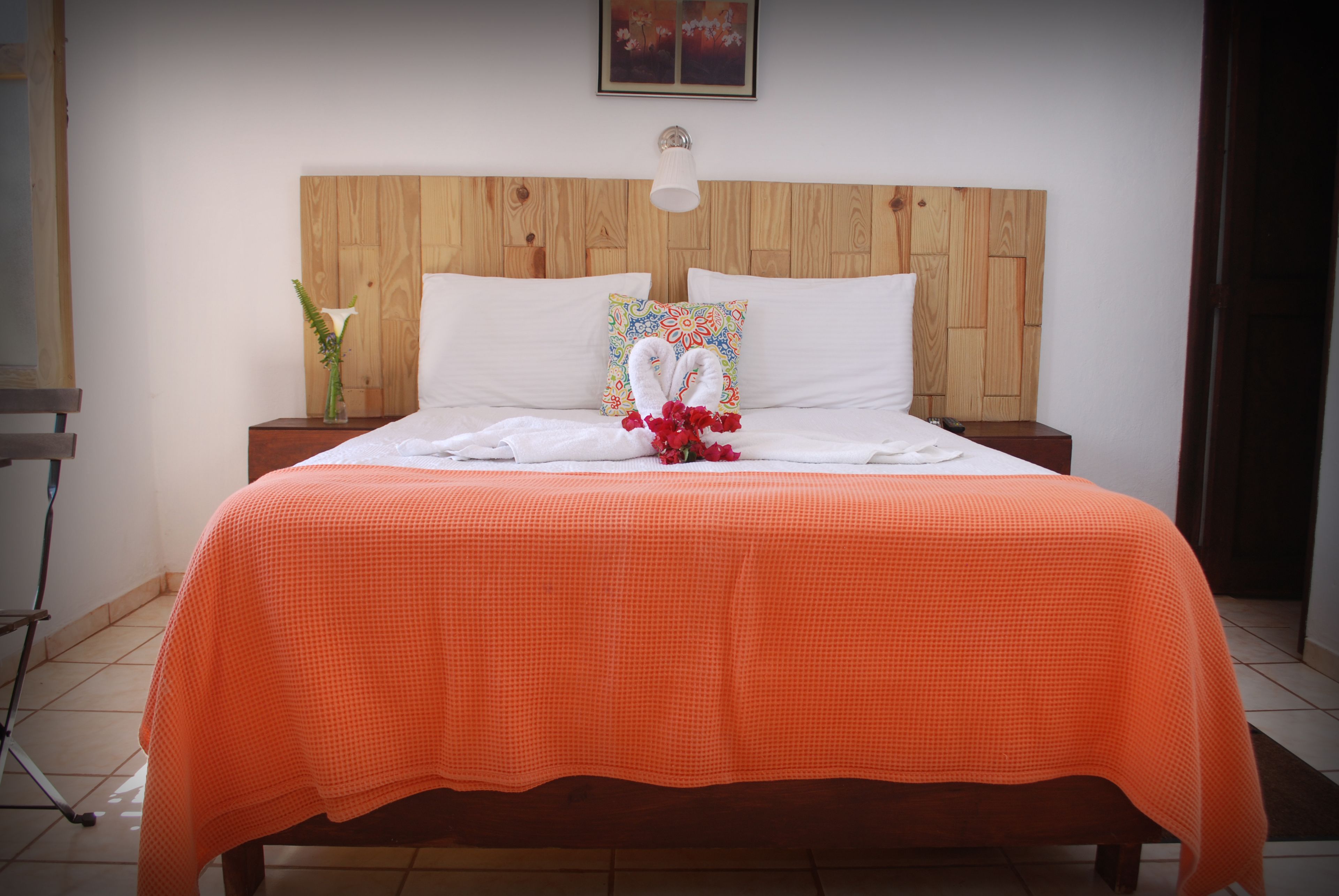 A neatly made bed with an orange bedspread, a wooden headboard, and a bedside table with a vase of flowers.