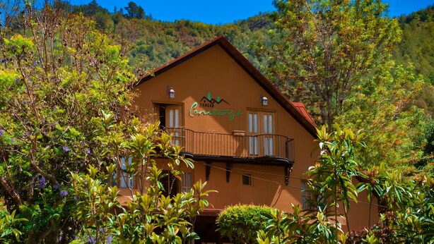 A two-story building with a balcony, surrounded by lush greenery and hills in the background.