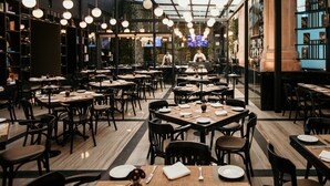 Um restaurante moderno com várias mesas e cadeiras, um cozinheiro ao fundo e teto de vidro.