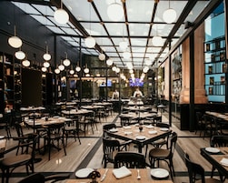 Un ristorante moderno con diversi tavoli e sedie, uno chef sullo sfondo e un soffitto in vetro.