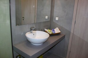 A modern bathroom with a white sink, a mirror, and a basket of toiletries on the countertop. - Mulberry Suites (Rhodes)