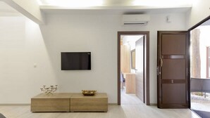 Un salon moderne avec un téléviseur à écran plat fixé au mur, une console en bois et une porte donnant sur une autre pièce.