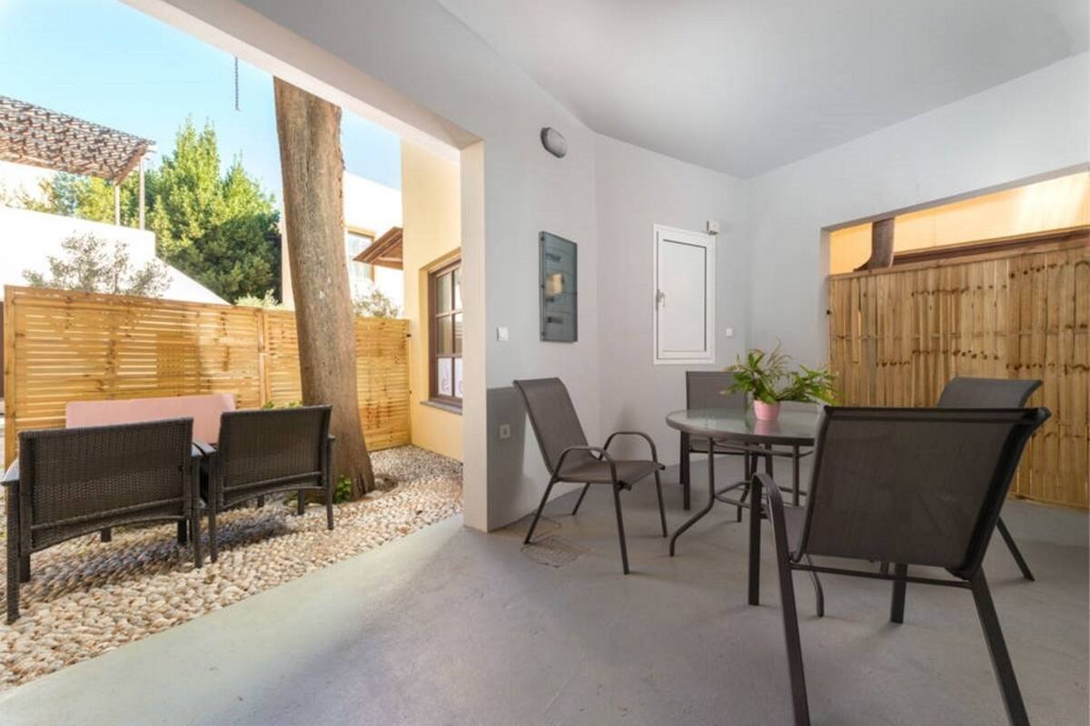 Un patio al aire libre con una mesa, sillas, una cerca de madera y un árbol.