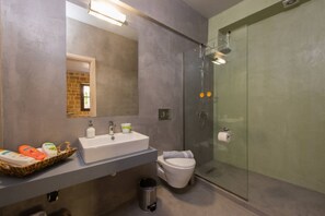A modern bathroom with a large mirror, a white sink, a glass shower enclosure, and a toilet. - Mulberry Suites (Rhodes)