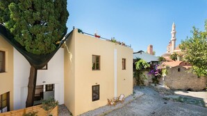 Une cour avec un sol en pierre, un arbre et un bâtiment à la façade beige et aux fenêtres.
