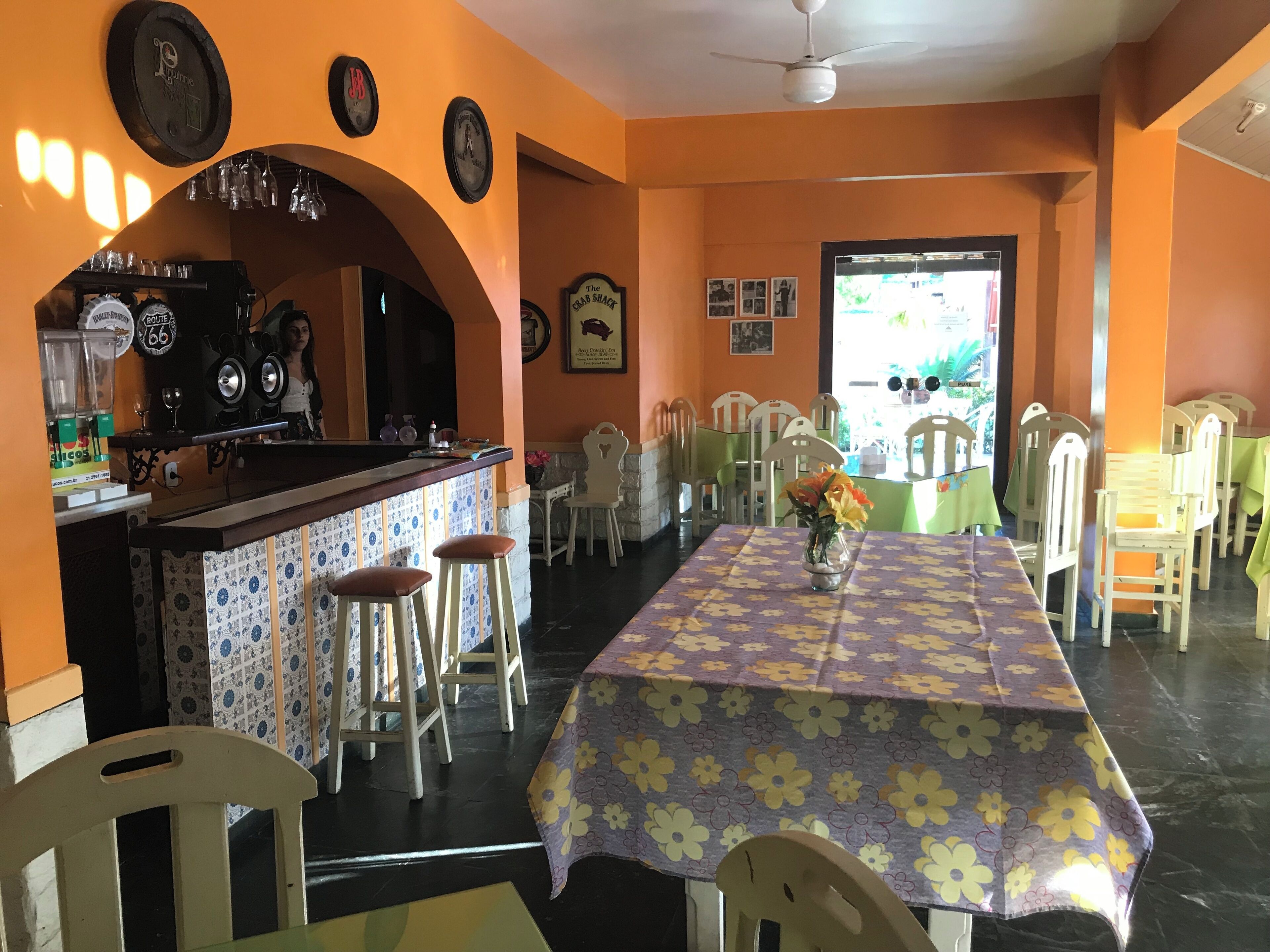 Um restaurante com uma mesa comprida, cadeiras, área de bar e vista através de uma porta.