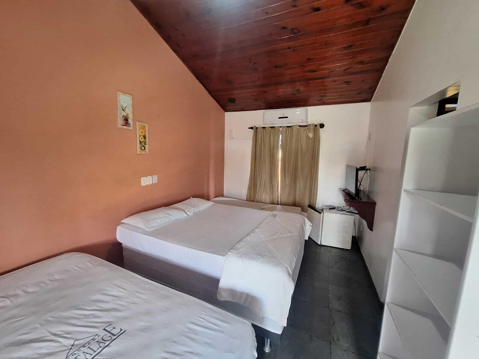 Um quarto pequeno e acolhedor com duas camas, teto de madeira e uma escrivaninha simples.
