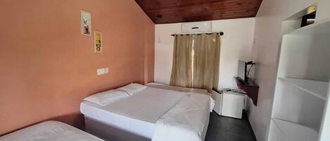 Um quarto pequeno e acolhedor com duas camas, teto de madeira e uma escrivaninha simples.