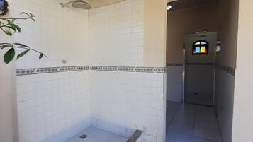 A tiled bathroom with a shower area, a small window, and a stone floor.
