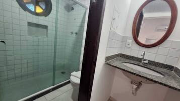 Un baño con ducha de vidrio, inodoro y lavamanos con espejo.