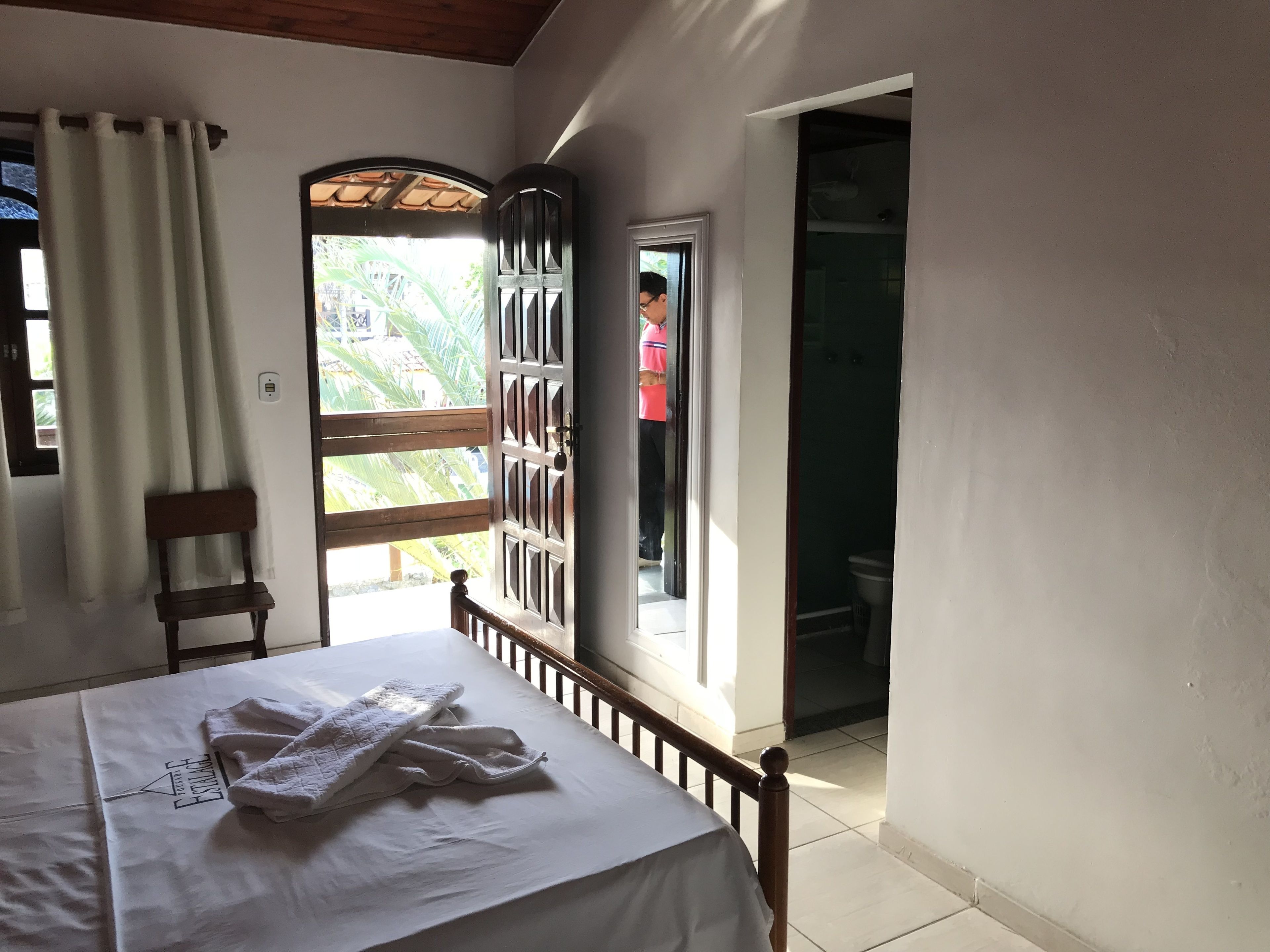 Une chambre à coucher avec un lit, une chaise, une fenêtre avec des rideaux et une porte donnant sur l’extérieur.