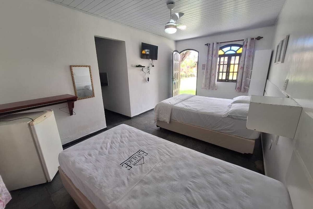 Ein Hotelzimmer mit zwei Betten, einem kleinen Kühlschrank, einem Spiegel und einem Deckenventilator.