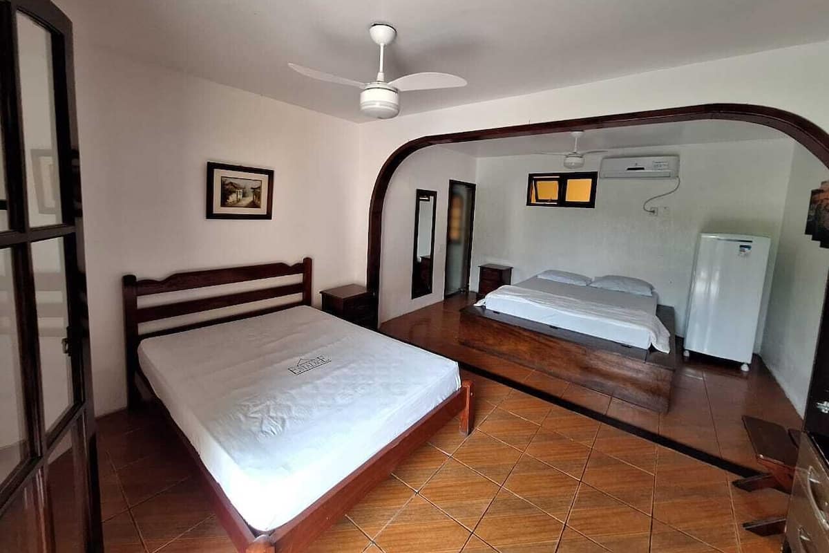 Ein Schlafzimmer mit einem Einzelbett, einem Holz-Kopfteil, einem Deckenventilator und einer weißen Wand-Klimaanlage.