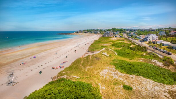 A beach with a clear view of the ocean, a sandy shore, and a row of houses along the coastline. - Stunning beach views on Over the Dunes - White Horse Beach, Plymouth (Plymouth)