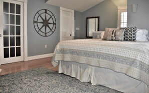 A bedroom with a bed, a large wall clock, a mirror, and a door.
