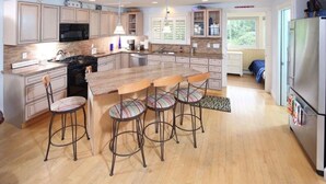 A modern kitchen with a central island, bar stools, and a refrigerator. - Stunning beach views on Over the Dunes - White Horse Beach, Plymouth (Plymouth)