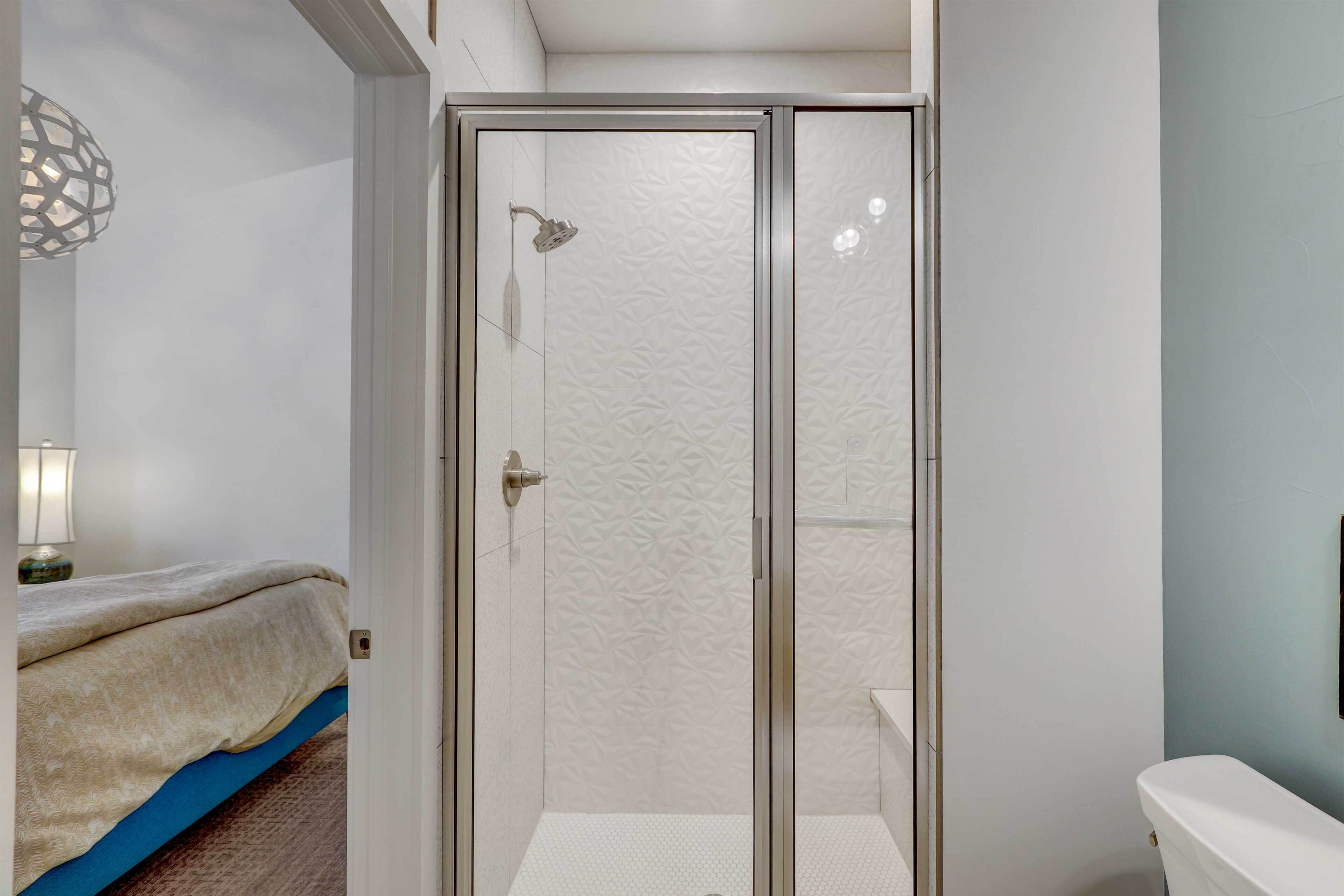 A bathroom with a glass-enclosed shower, a toilet, and a bed with a blue mattress.