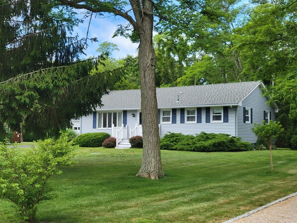 A single-story house with a front porch, surrounded by a well-maintained lawn and mature trees.