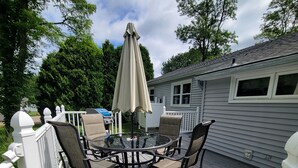 Een terras met een ronde glazen tafel, vier stoelen, een parasol en een witte balustrade.