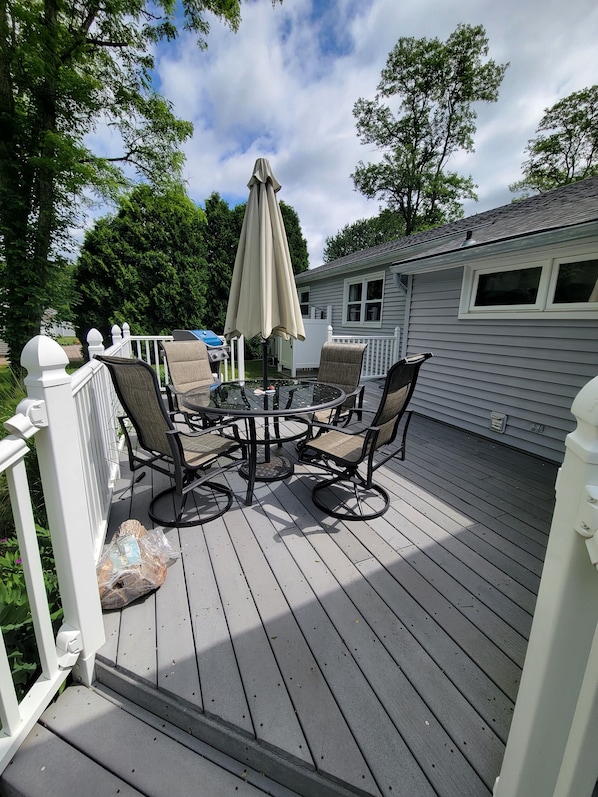 A deck with a round glass table and four chairs, an umbrella, and a white railing. - Conveniently located in a private association very close to beaches. (Charlestown)