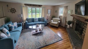 Een woonkamer met een blauwe bank, een geruit fauteuil, een salontafel en een open haard.