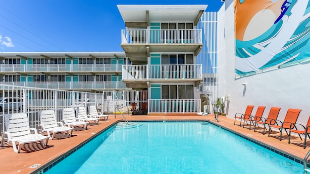 A swimming pool with lounge chairs, a multi-story building with balconies, and a mural on the side. - Surf Inn Suites (Ocean City)