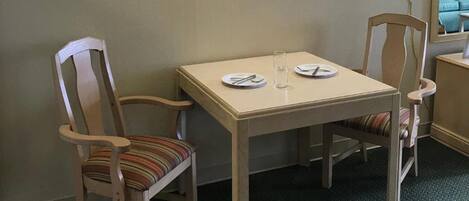 A small hotel room with a single table and two chairs, a bed with a floral bedspread, and two wall-mounted lamps.