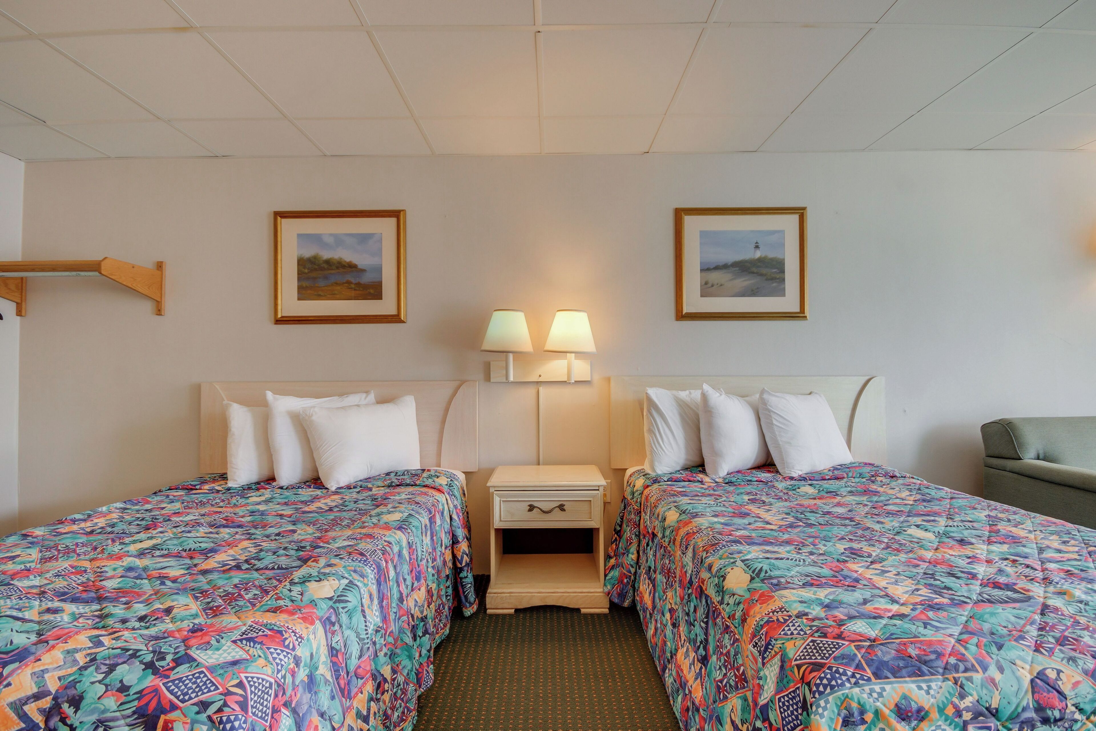 Ein Hotelzimmer mit zwei Betten, einem Nachttisch mit Lampe und gerahmten Bildern an der Wand.