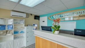 A reception desk with a surfboard sign, a potted plant, and a computer. - Surf Inn Suites (Ocean City)