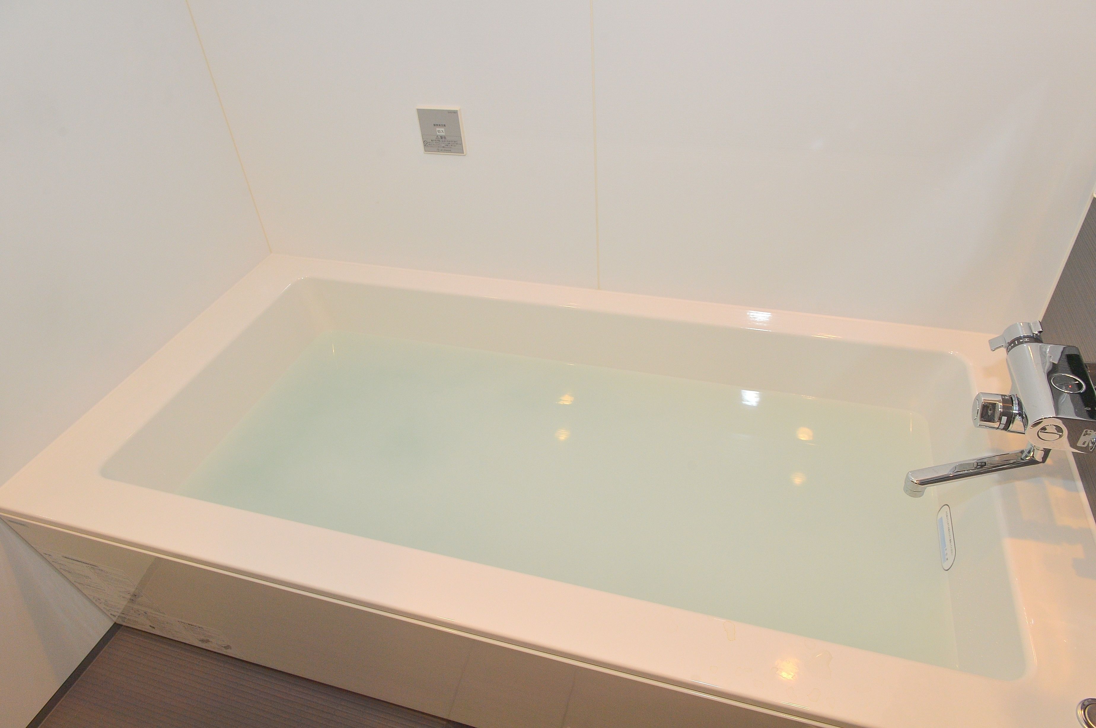 Una bañera rectangular con un grifo de cromo y un panel de control en la pared.