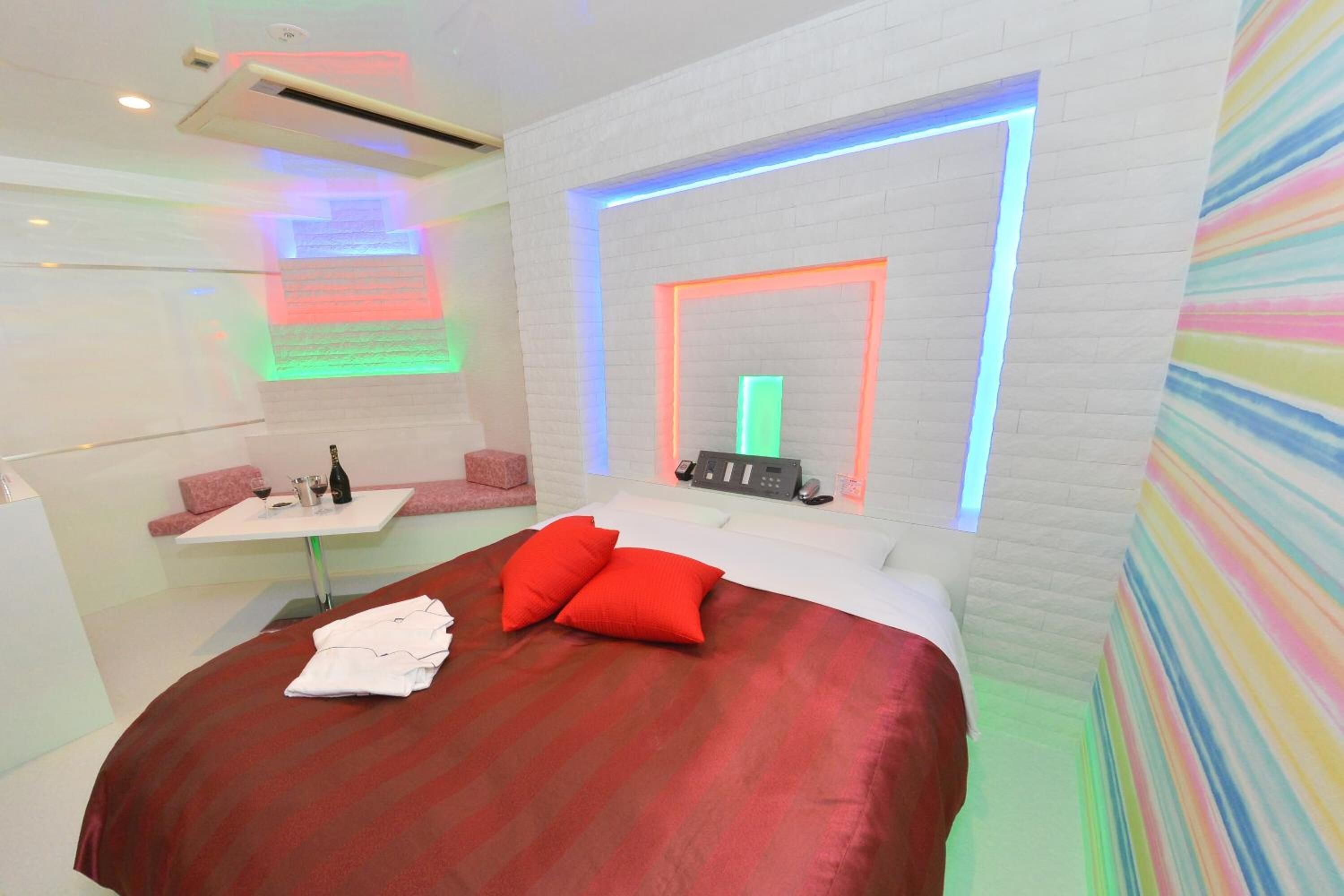 Una habitación de hotel moderna con una cama grande, una mesita pequeña con una botella y vasos, un teléfono en la pared y una pared con rayas de colores.
