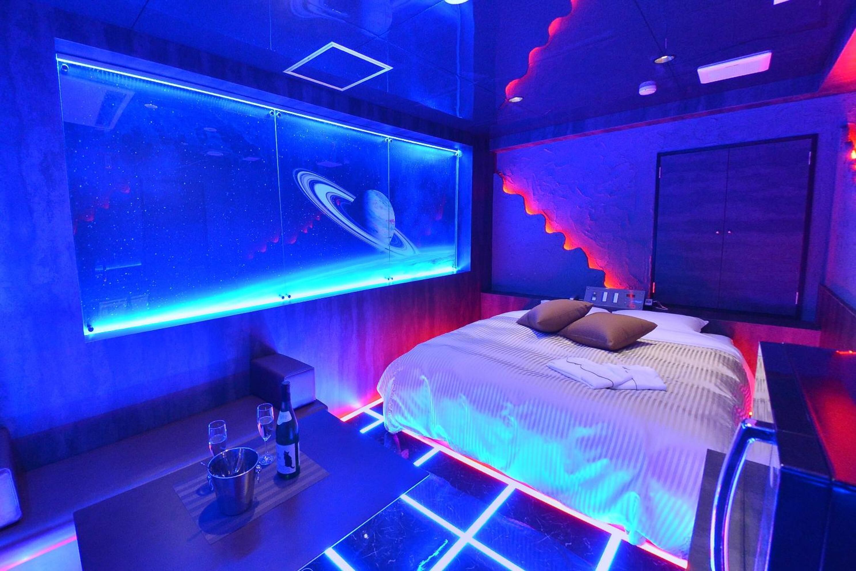 Une chambre moderne avec un grand lit, un téléviseur fixé au mur qui diffuse une image sur le thème de l’espace, et un éclairage d’ambiance.