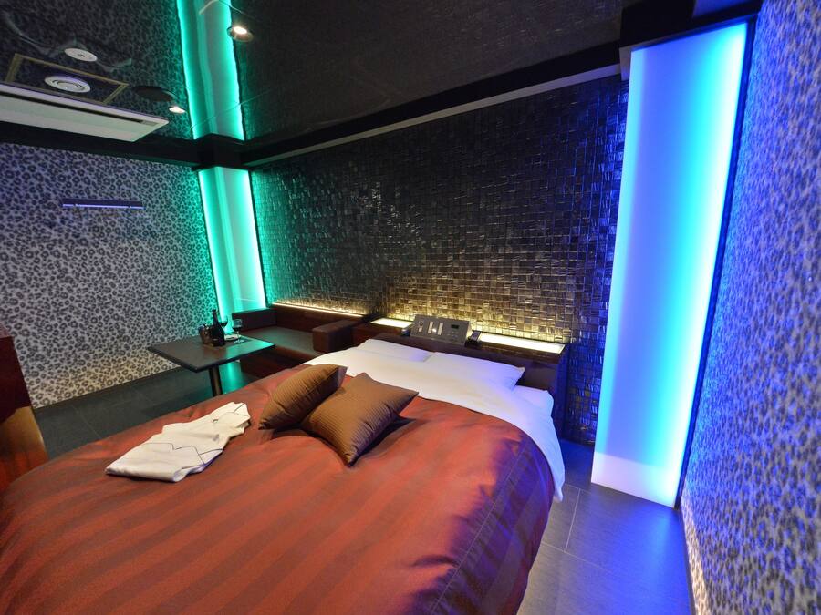A modern hotel room with a large bed, a nightstand, and a wall with a textured pattern.