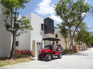 A red golf cart parked on a paved street in a residential area with white buildings and green trees.