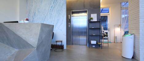 Un área de recepción moderna con pared de mármol, un mostrador de recepción, un ascensor y un pequeño espacio con asientos.