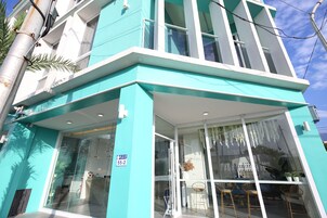 Um edifício moderno com fachada azul-turquesa, janelas amplas e entrada visível.