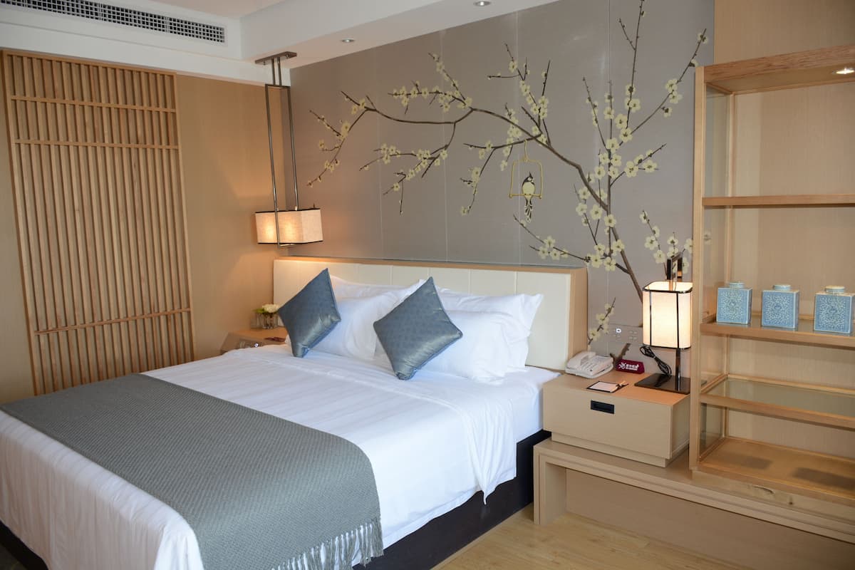 A neatly made bed with pillows, a bedside lamp, and a small bedside table with a phone and a decorative item.