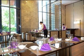 A restaurant with tables set for dining, a waiter attending to guests, and a view of the outdoors through large windows. - Shanshui S Hotel Maliandao (Beijing)