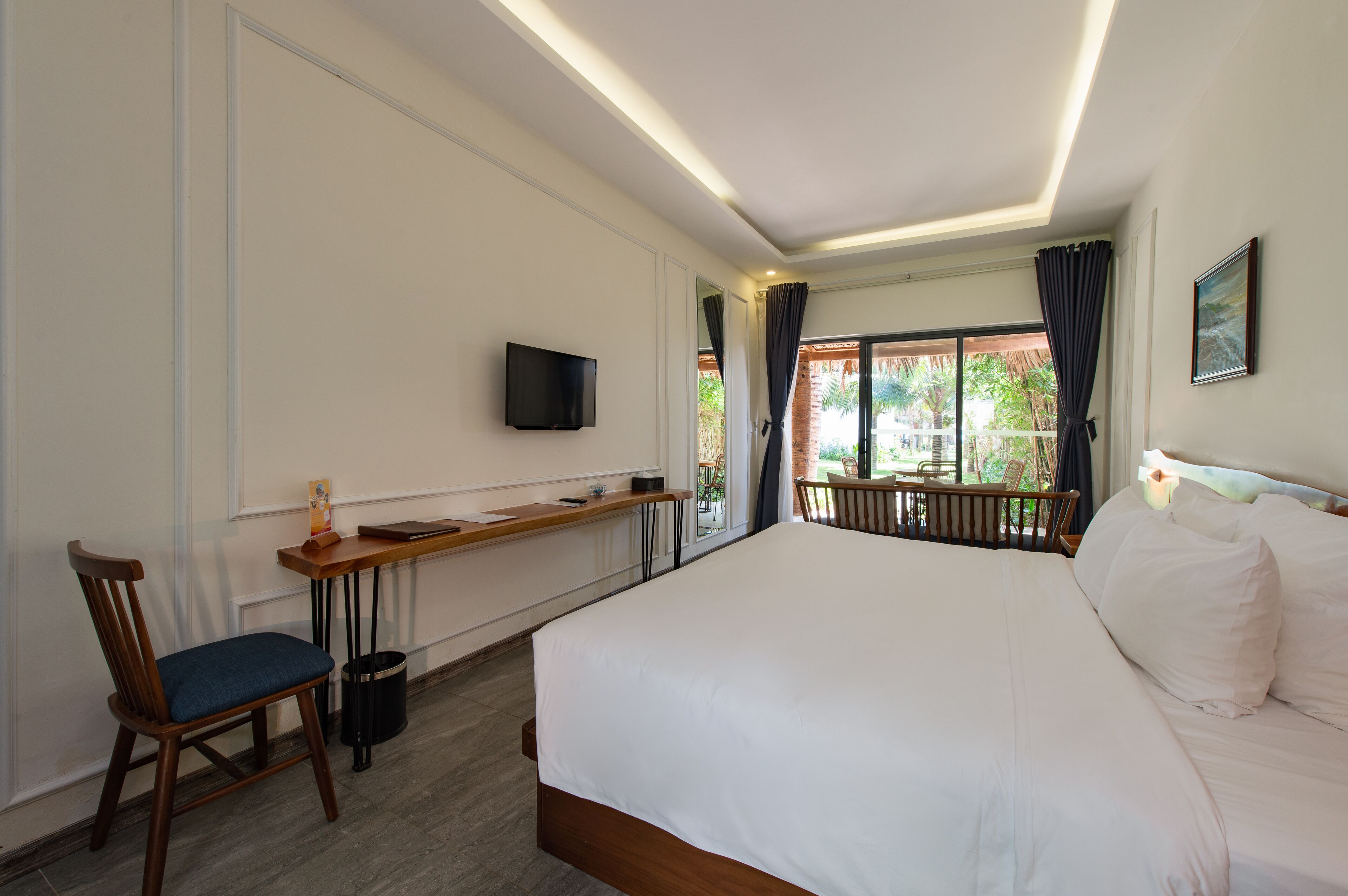 Habitación de hotel con una cama grande, un escritorio con silla, televisión y ventana con cortinas.