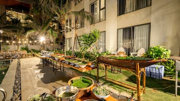 A poolside dining area with tables set for meals, surrounded by palm trees and a building with large windows.
