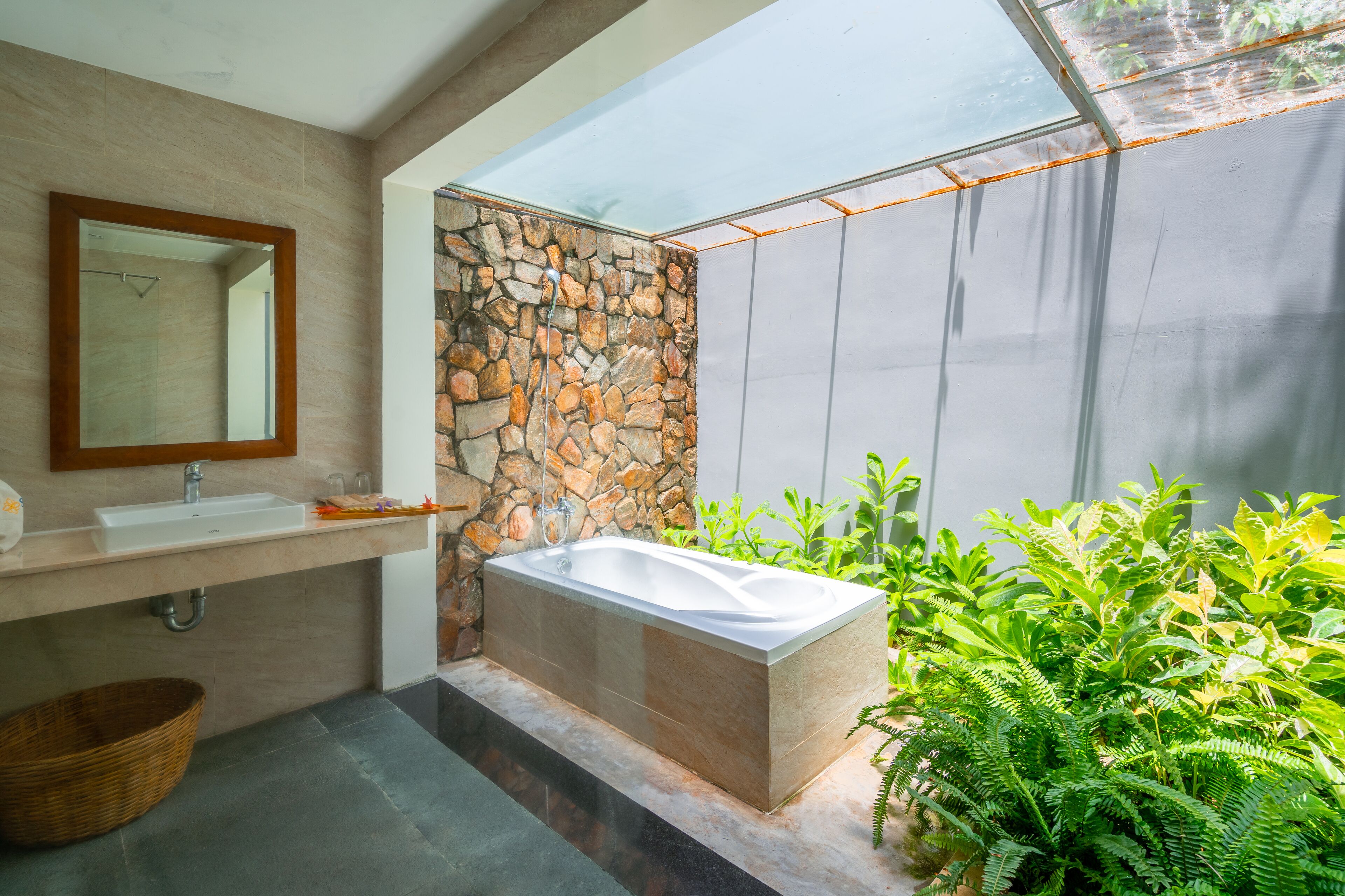 A modern bathroom with a stone wall, a freestanding bathtub, a large mirror, and a sink with a basket.