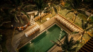 An aerial view of a resort with a swimming pool, dining area, and palm trees.