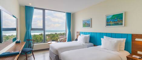 A hotel room with two beds, a desk, a chair, a TV, and a large window with a view of the ocean.